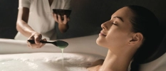 Female having a warm bath and therapist putting essences in the water