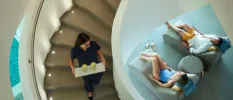 Female staff member carries a tray of drinks down a winding staircase to a couple relaxing on daybeds below