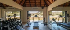 Gym with a wood-beamed ceiling and floor-to-ceiling windows, equipped with treadmills, benches, bikes and weights