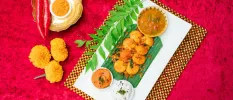 Orange coloured food laid out next to orange flowers and a leaf on a white plate