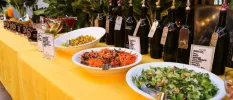 Bowls of salads and juices lined up on a long table with a yellow table cloth
