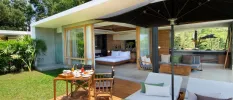 Villa with wooden furnishings, a bed overlooking the jungle and an outdoor terrace with a table and chairs and white cushioned loungers