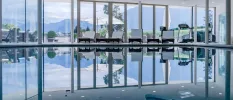 Indoor pool surrounded by white-cushioned loungers with floor-to-ceiling windows showcasing the mountains beyond
