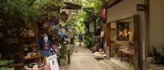Woman walks down a tropical pathway with two stores selling handwoven baskets, hats and resort wear