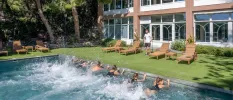 Group in black swimwear hold onto the side of a pool and kick their legs as part of a group class