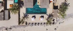 Aerial view of Six Senses Zighy Bay, including grey rooftops, palm trees, an infinity pool and orange loungers, all set in ivory sands