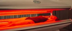 Female in a black swimsuit lies in a lounger with red infrared lighting