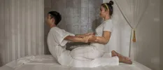 Woman lies on her front as a therapist pulls her backwards by her arms, aiding a stretch