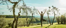 Woman in black active wear in a yoga pose outdoors overlooking vineyards and olive groves