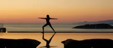 Silhouette of a woman in a yoga pose at sunrise or sunset next to an ocean-facing pool