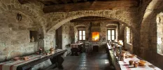 Restaurant with stone walls and ceiling and wooden beams, with a lit fireplace at one end