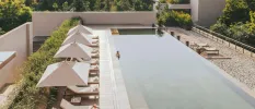 Man relaxes in a rectangular swimming pool lined with smart white-cushioned loungers and parasols