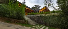 Stone pathways leading to a garden area and a building lit up at twilight, with stone and wood exteriors and a triangular roof