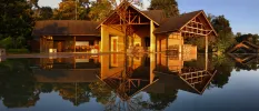 Lake-like swimming pool under a blue sky among tropical greenery, overlooked by a wooden building with triangular rooftops and stilts