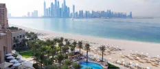 Palm-lined pool and sandy beach looking across the sea to the Dubai skyline