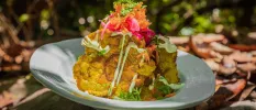Vegetable fritters piled high with a salad topping and white dressing, served in a tropical garden setting