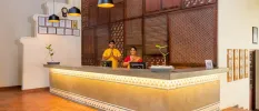 Staff in traditional Indian dress smile with their hands clasped behind an LED-lit reception desk, with a dark-wood carved wall behind