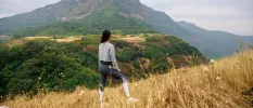 Woman stands on a hillside in active wear, gazing out towards forested peaks