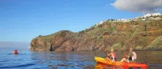 Two people in a yellow and red canoe paddling past a rocky outcrop under a blue sky