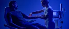 Medical team member inserts an IV into a man's arm with red light technology, in a darkened blue-lit room