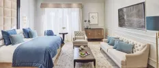 Hotel bedroom with blue cushions and a throw, a beige sofa, wooden coffee table and padded beige velvet headboard