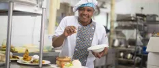 Smiling chef in uniform seasoning a dish in his kitchen