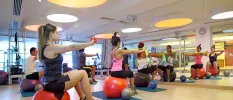 Group in active wear sit on red exercise balls in a studio with a large mirror