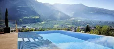 Infinity pool with a wooden deck and cypress tree overlooking mountains and valleys under a sunny sky