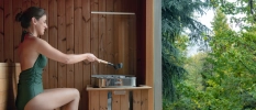 Lady in a green swim suit sitting in a sauna with views of the forest 
