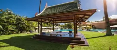 Wooden open-sided cabana with an Asia-style rooftop in a sunny garden with a lawn and swimming pools