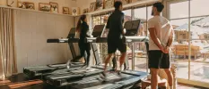 Man and woman in activewear run on treadmills in a bright studio, watched over by a fitness professional