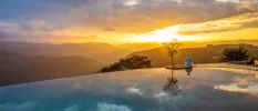 Infinity-edge pool at sunset, with mountains in the distance and a guest meditating on the edge
