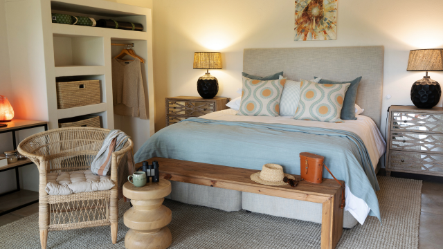 Hotel bedroom with wooden furniture and blue bedding, black bedside table lamps, a rattan chair and white wardrobe