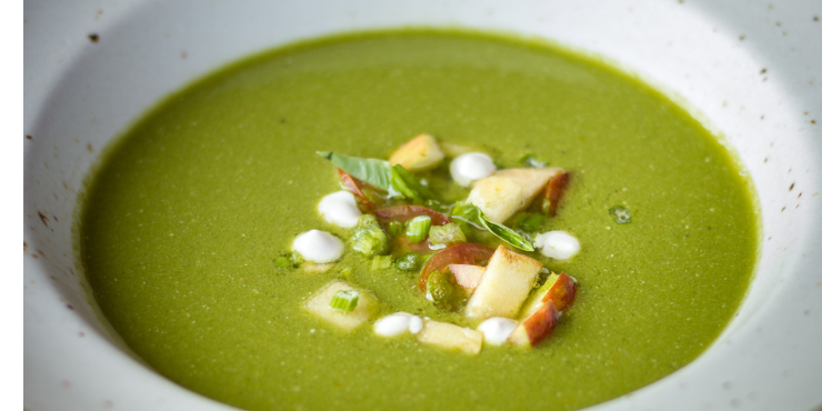 Thick green soup in a white bowl, garnished with green herbs and mushrooms