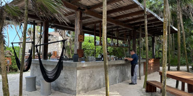 Concrete bar with a thatched roof and black hammocks, with timber benches nearby