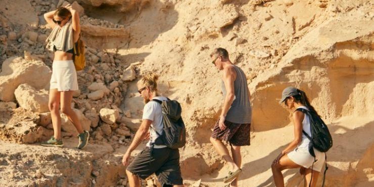 Group of men and women in active wear hike along a rocky path in the sunshine