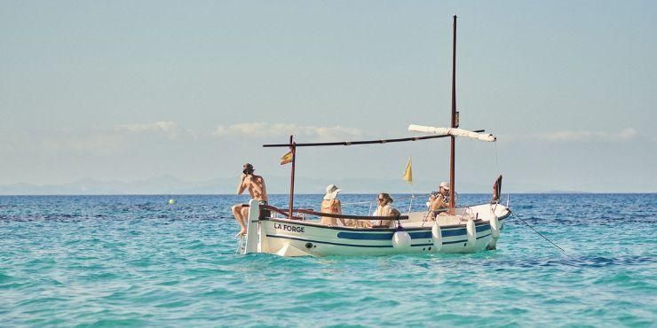 Group of people in swimwear on a boat floating in the sea, one about to jump off with a snorkel on