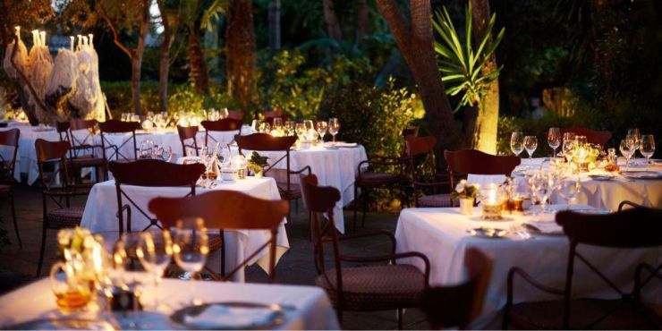 Elegant restaurant with red patterned curtains and chairs, white tablecloths and an open grill with mosaic tile design