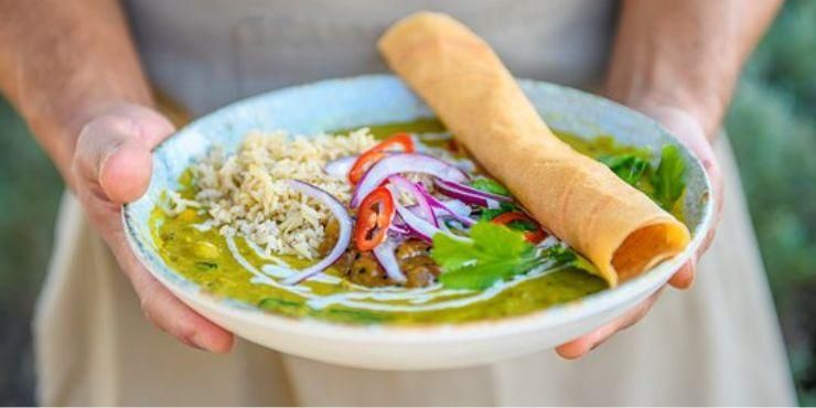 Person holds a plant-based meal of rice, red onion, peppers and a green curry sauce