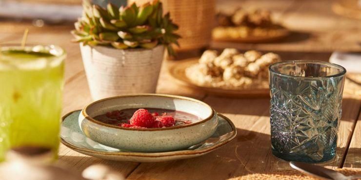 Rustic wooden table with a potted plant, green cocktail-like drink and bowl with puree and raspberries