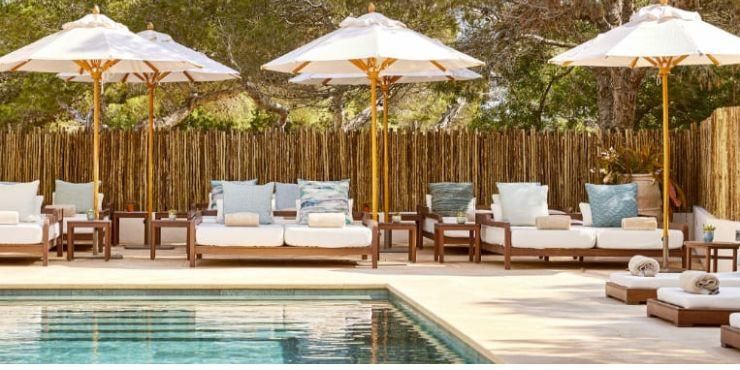 Swimming pool surrounded by wooden panelling and pine forests, with white-cushioned loungers on a sunny terrace