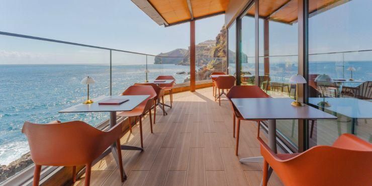 Stylish lounge area with neutral and yellow cushions, floor-to-ceiling windows and views of the ocean and rugged cliffs
