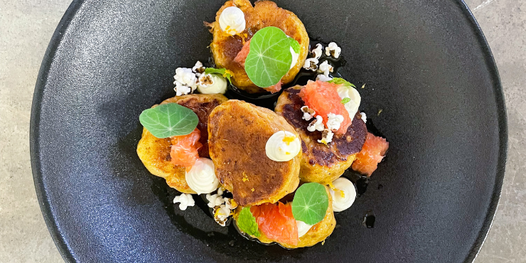 Round black plate topped with circular vegetables, tomatoes, herbs and dollops of white sauce