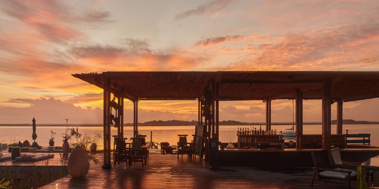 Our Habitas Bacalar bar at sunset, with a wooden deck and structure and lagoon view