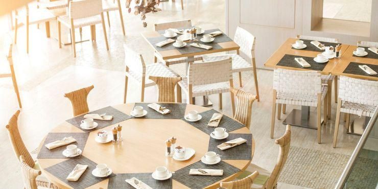 Wooden tables and chairs in a restaurant with floor-to-ceiling windows and sheer white curtains